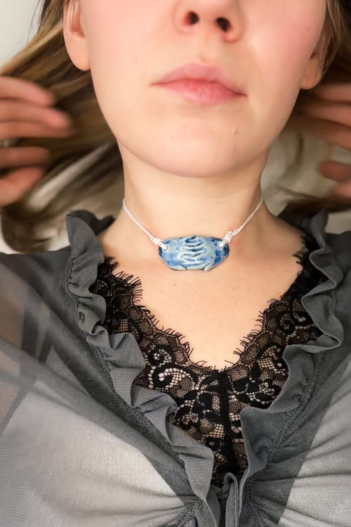 Woman wearing a gray sheer top with lace details and a blue ceramic necklace.
