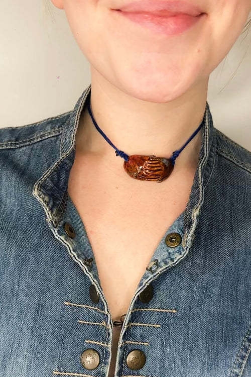 Person wearing a blue denim jacket with a necklace featuring a brown pendant.