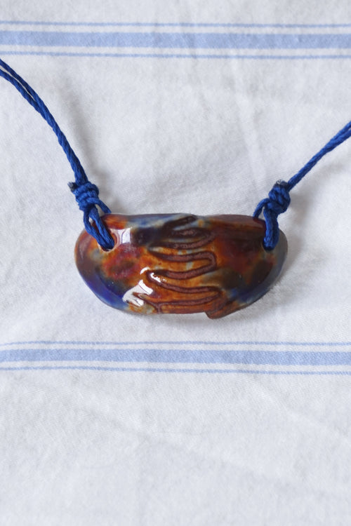 Brown pendant on a blue cord against a white background with blue stripes