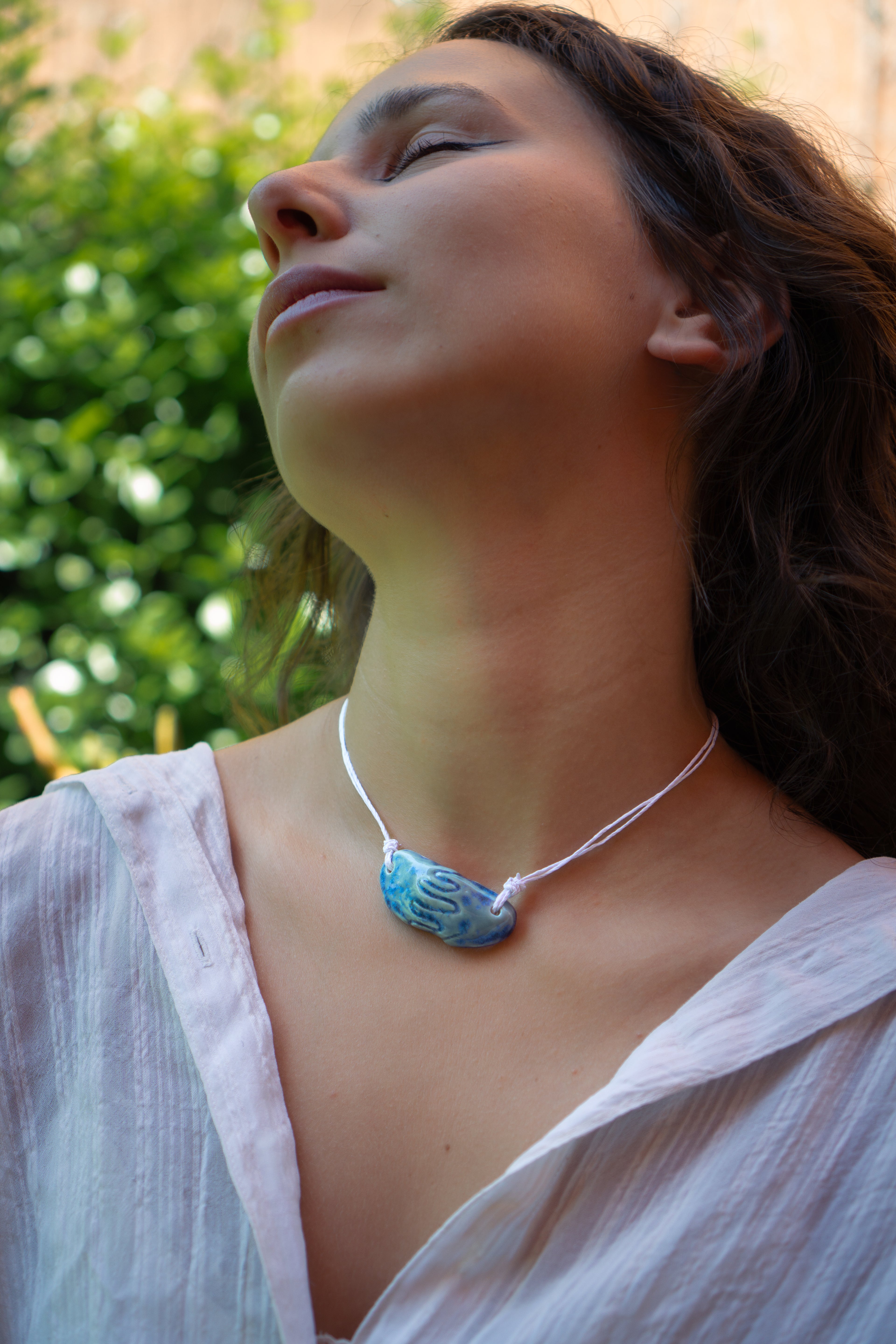 Girl with brown curly hair wearing a light blue ceramic necklace with a pendant replicating holding hands. Princess style necklace.