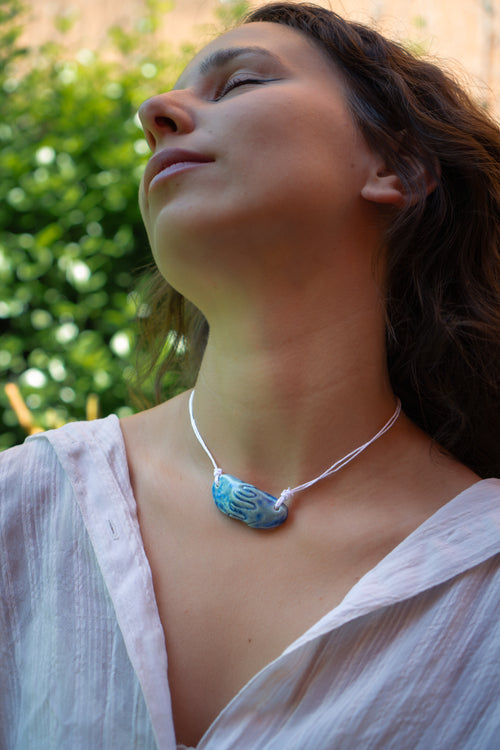 Girl with brown curly hair wearing a light blue ceramic necklace with a pendant replicating holding hands. Princess style necklace.