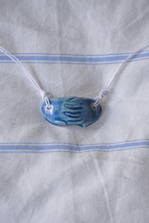 Blue ceramic pendant on a white cord against a white fabric background with blue stripes