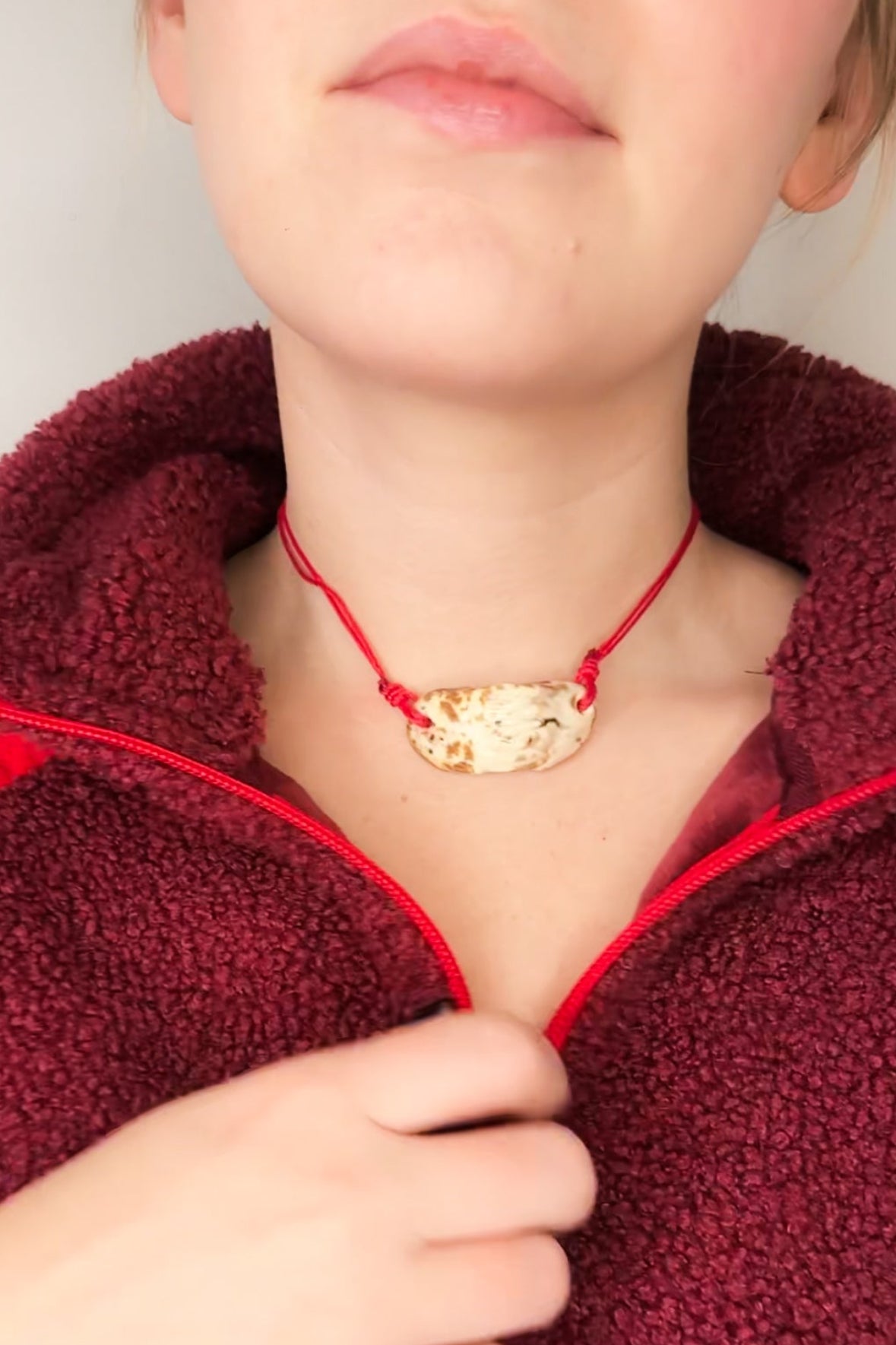 Person wearing a red jacket with a cow print ceramic necklace with red cord.