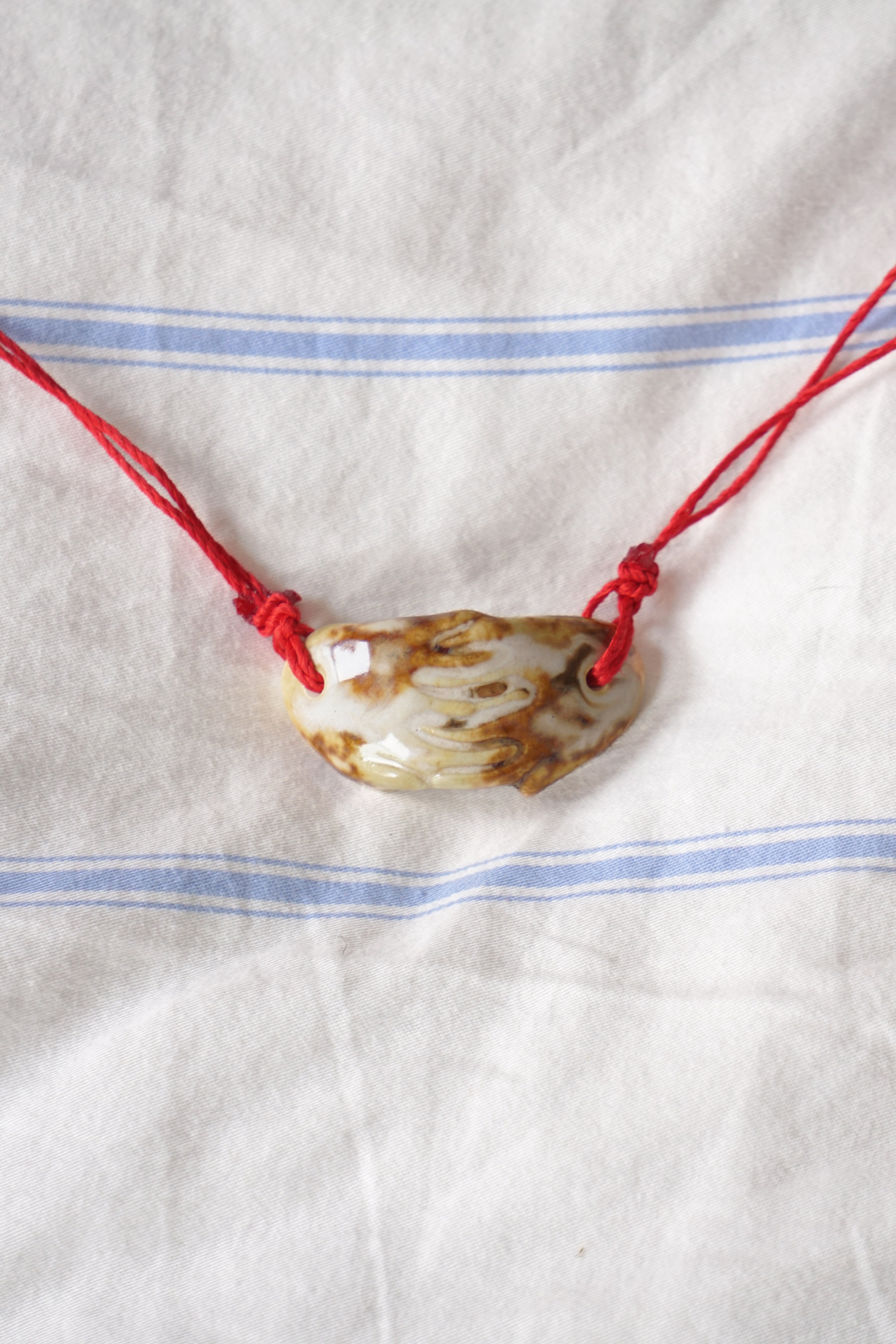 cow print ceramic necklace with red cord against a white fabric background