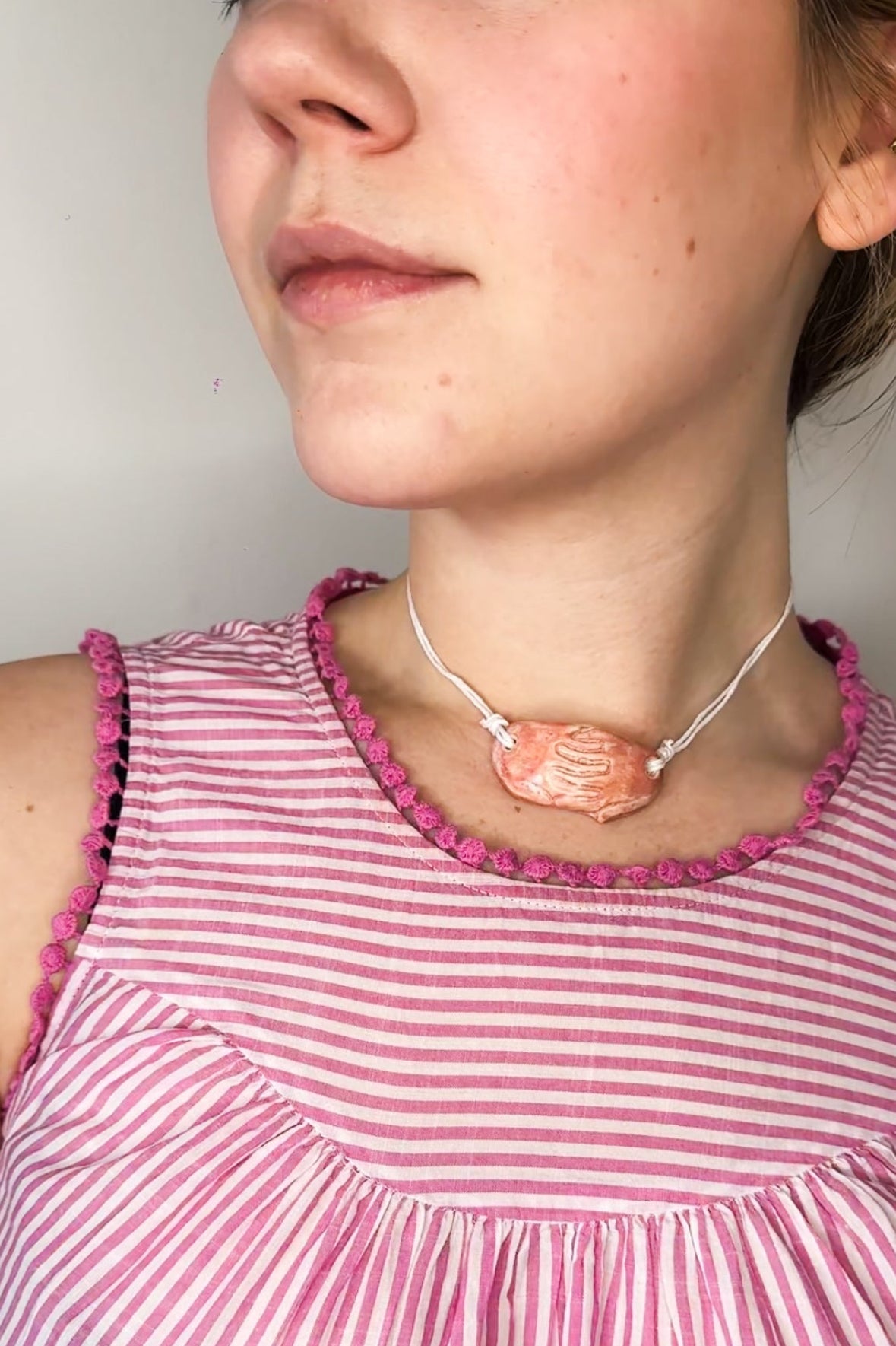 Person wearing a pink and white striped dress with a necklace.