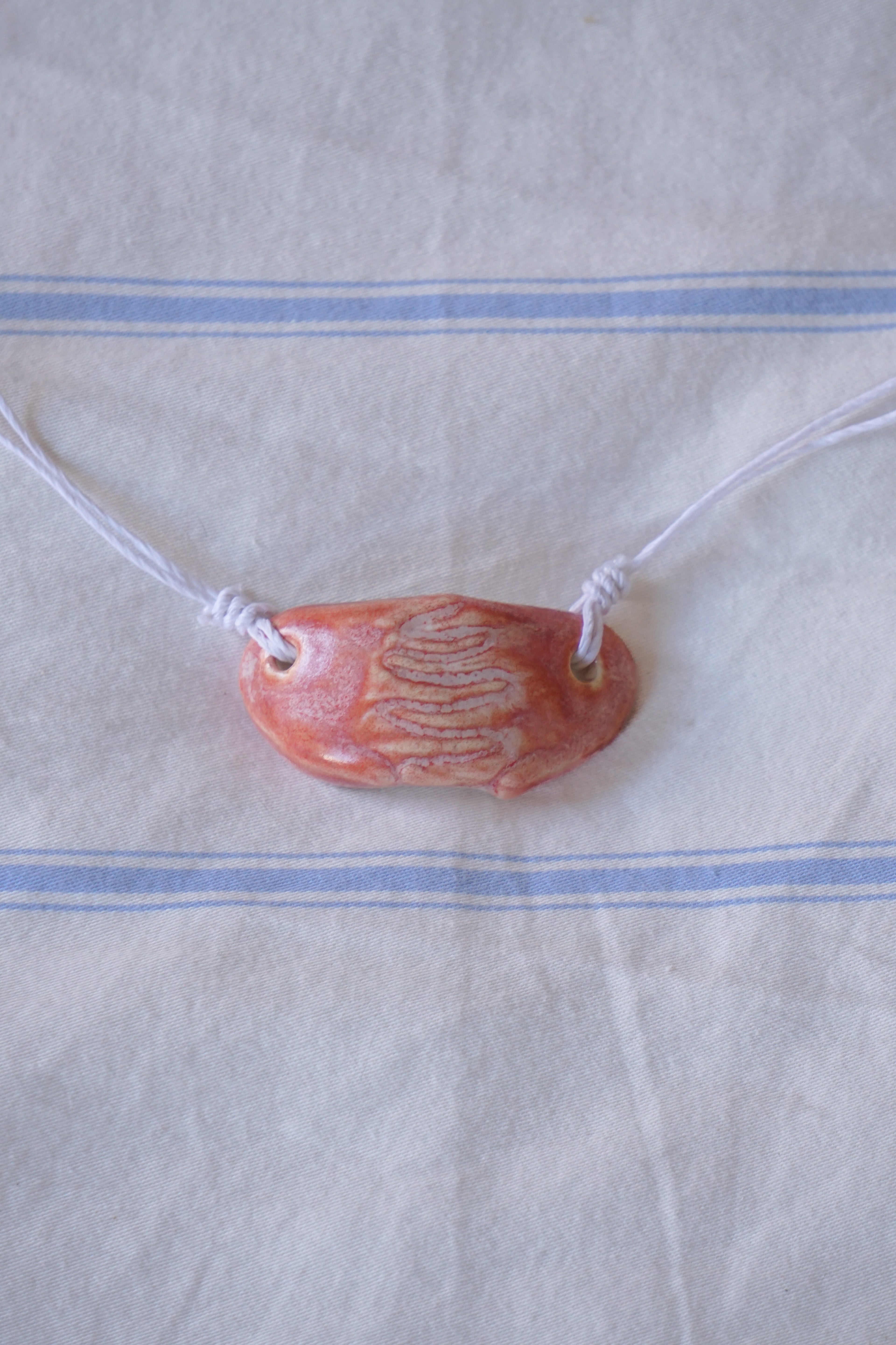 Necklace with a coral colored, handmade ceramic pendant on a white fabric background